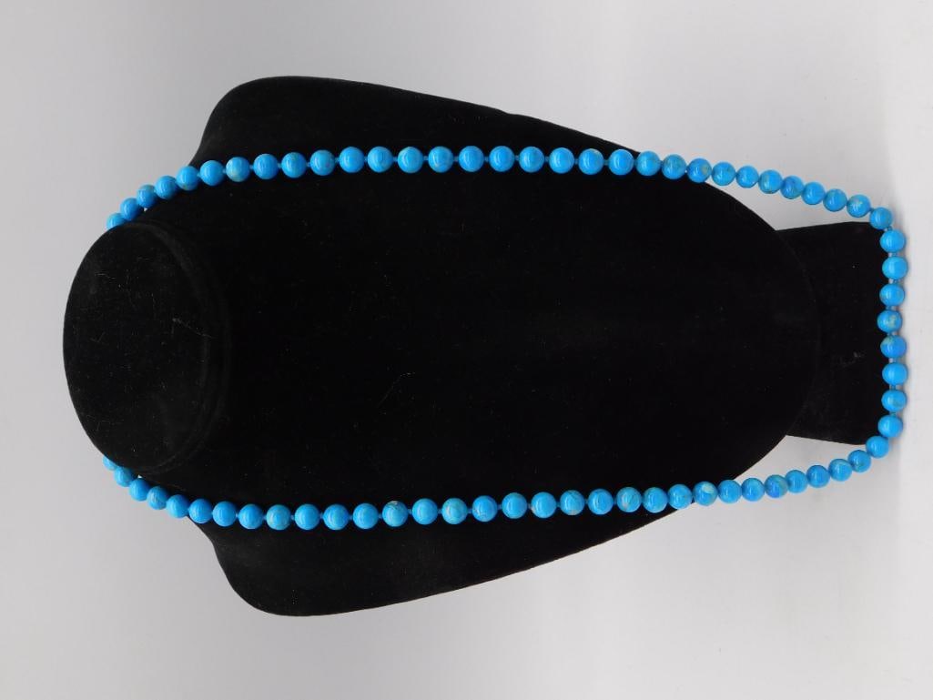 Turquoise Beaded Necklace: A single strand necklace of round turquoise-colored beads, approximately 6-7mm each, displayed on a black velvet bust. The necklace measures roughly 30 inches in length as shown with a ruler. Beads