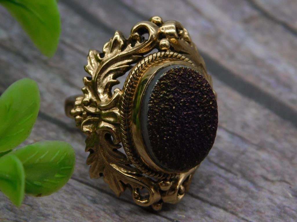 Gold-Tone Statement Ring with Dark Drusy Stone, Marked India: Ornate gold-tone costume ring with a scrolling leaf and floral design surrounding a large oval dark purple/black drusy-style cabochon, size 7. The interior shank is stamped "India" along with addition