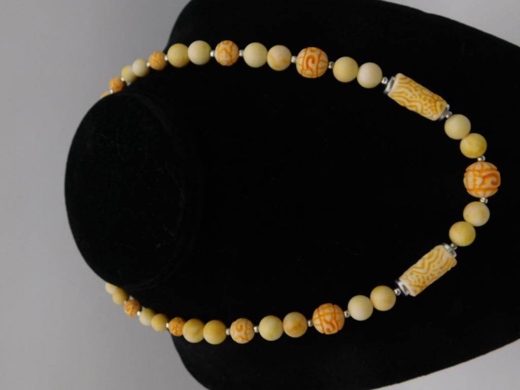 Carved Yellow Jade-Style Beaded Necklace: Beaded necklace featuring round yellow and orange carved beads with scrollwork and geometric patterns interspersed with smooth cylindrical and spherical beads, silver-tone spacer accents throughout. D
