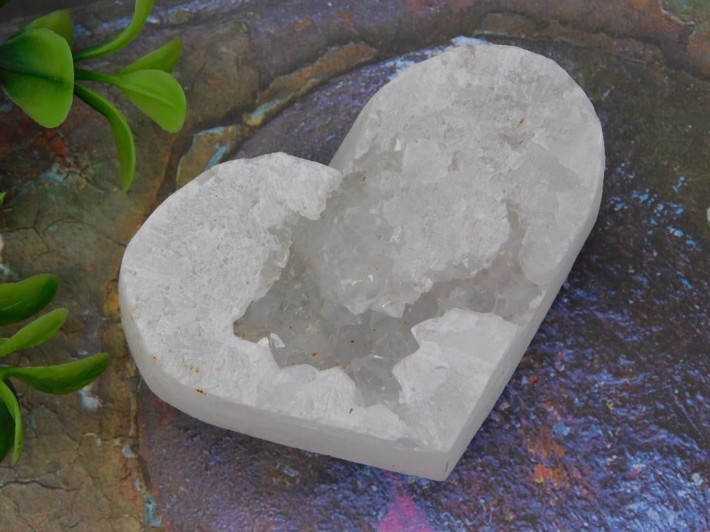 Crystal Geode Heart - White Quartz Druzy Carved Specimen: A heart-shaped carved white quartz geode specimen with a sparkling druzy crystal-filled cavity at center. Shown on an iridescent stone slab beside a 1966 Liberty quarter, with an auction lot card noti