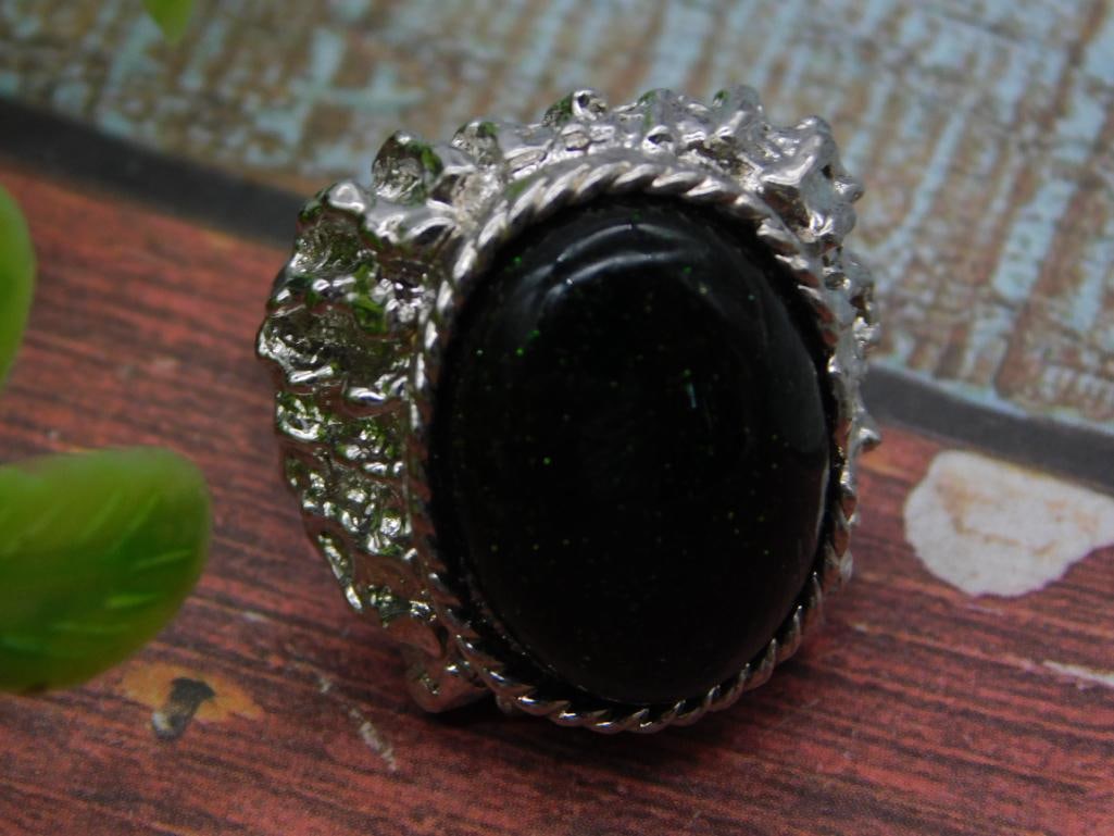 Jewelry - Black Stone Cocktail Ring in Ornate Silver-Tone Setting: A statement cocktail ring featuring a large oval black cabochon stone (onyx or obsidian) set in a textured, nugget-style silver-tone metal mounting with a rope-twist border. Photographed beside a 1966