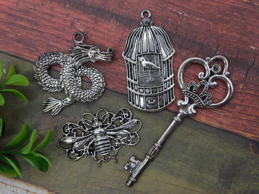 Jewelry Charm Pendant Lot - Dragon, Birdcage, Key, and Bee Designs: Group of four silver-tone metal jewelry pendants/charms including an ornate dragon, a birdcage with perched bird, a large skeleton-style key with heart and crown scrollwork, and a filigree bee. A 1966