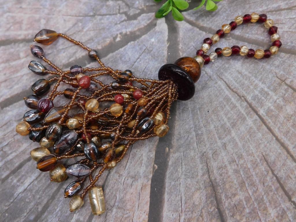 Beaded Tassel Pendant with Mixed Glass Beads and Wood Bead Accent: Ornate handmade beaded tassel featuring mixed amber, garnet, and iridescent glass beads netted around bronze seed beads, topped by a dark lacquered wood bead and a beaded loop of garnet, citrine, and