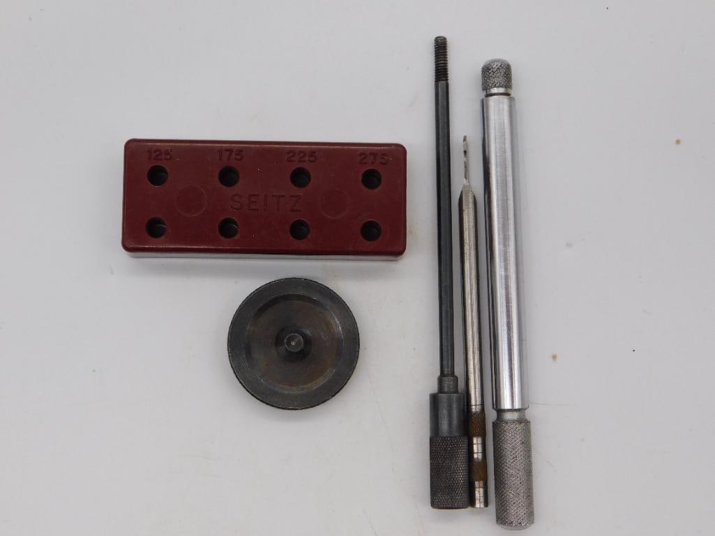 Seitz Jeweling Tool Set with Punch Block: A Seitz brand watchmaker's jeweling tool set including a burgundy punch block numbered 125, 175, 225, and 275, a round steel anvil disc, and three graver or reaming hand tools with knurled handles. A