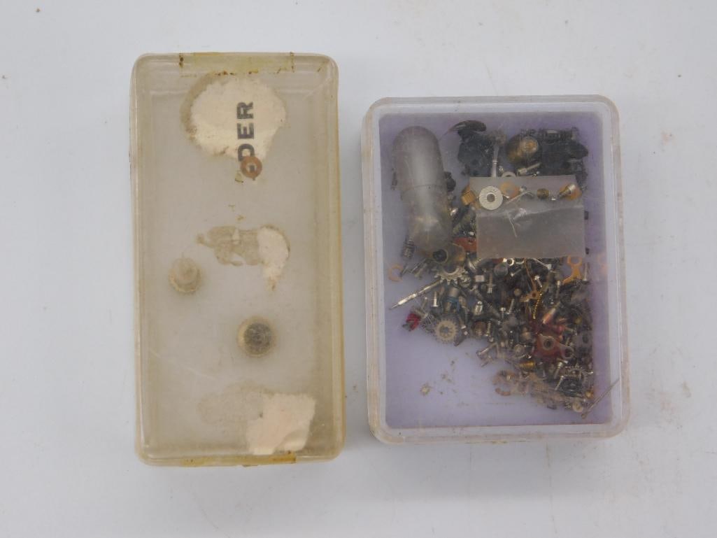 Antique Watchmaker Parts Storage Boxes, Pair: Two small plastic storage boxes used for organizing watch repair parts; one is largely empty with only a few small components remaining and residue from an old label, the other contains a dense