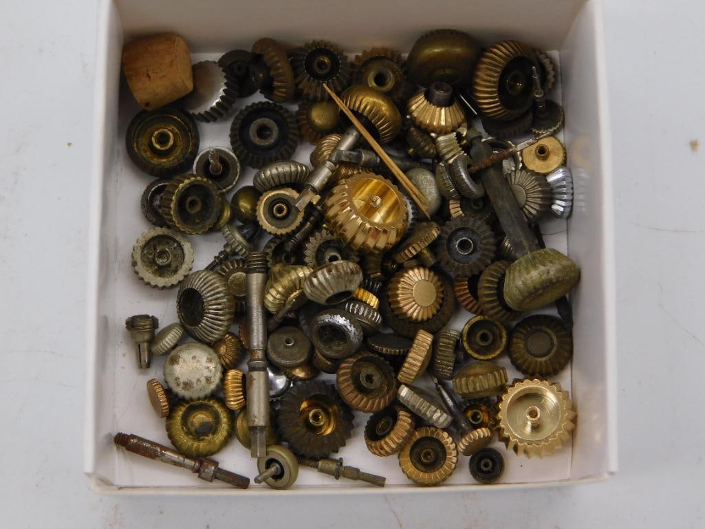 Antique Watchmaker Gear Parts Lot, Boxed: A cardboard box filled with a large assortment of small brass and steel gears, fluted knobs, and pinion pieces, including a cork stopper mixed in among the hardware. A quarter is shown for scale.