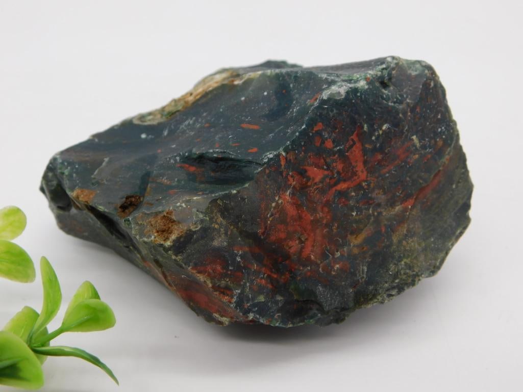 Natural Bloodstone Heliotrope Rough Mineral Specimen: A single rough, unpolished bloodstone (heliotrope) specimen showing characteristic dark green chalcedony with red iron-oxide inclusions. Auction tag lists weight as 1 lb 9 grams. Measures roughly 4