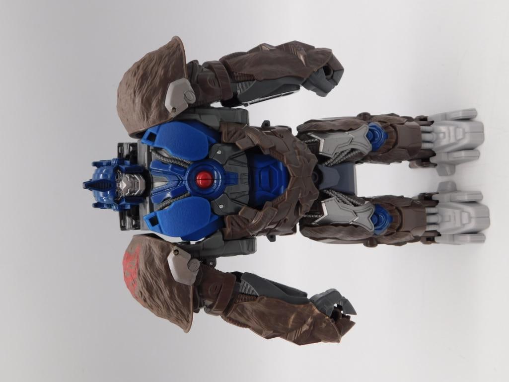 Transformers Optimus Primal Beast Wars Gorilla Action Figure: An articulated Optimus Primal-style Transformers action figure in gorilla/beast mode, finished in brown, gray, and blue with glowing green eye detail and a red Autobot-style insignia on the back.