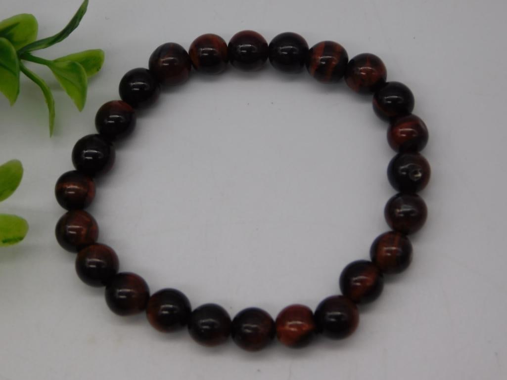 Red Tiger's Eye Beaded Stretch Bracelet: A stretch bracelet strung with polished red tiger's eye beads showing rich chatoyant banding in red, brown, and black. Measures approximately 7-7.5 inches around, shown with a quarter for scale.