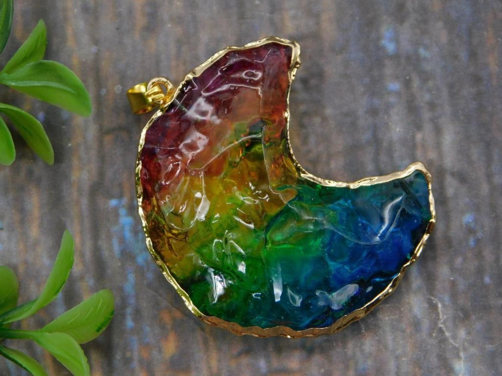 Rainbow Fused Glass Crescent Moon Pendant, Gold Trim: Handcrafted crescent moon-shaped pendant with vibrant fused resin/glass in a rainbow gradient of red, orange, green, and blue, edged in a hammered gold-tone bezel. Measures approximately 2 inches,