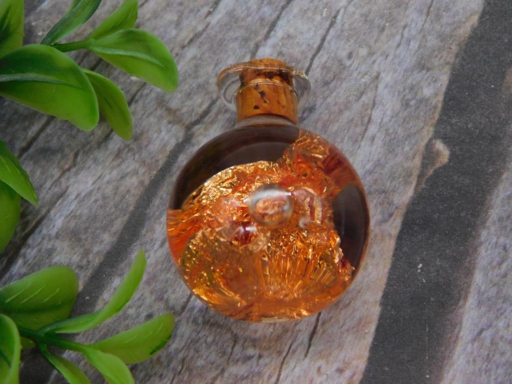 Amber Glass Foil-Art Perfume Bottle: A round amber/copper-toned art glass bottle with cork stopper containing decorative gold foil flake inclusions. Small size, approximately 1.5 inches.