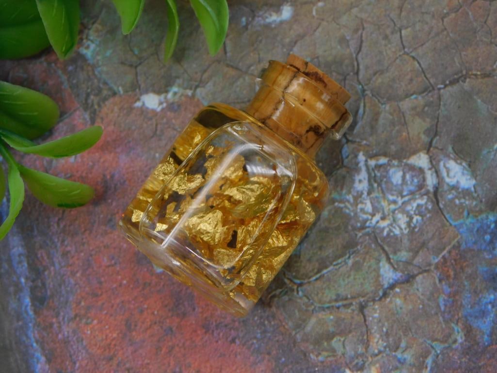 Gold Leaf Flakes in Corked Glass Bottle, Specimen Vial: Small glass bottle with cork stopper containing loose genuine gold leaf flakes, displayed on an iridescent stone slab. Approximately 1.5 inches tall.