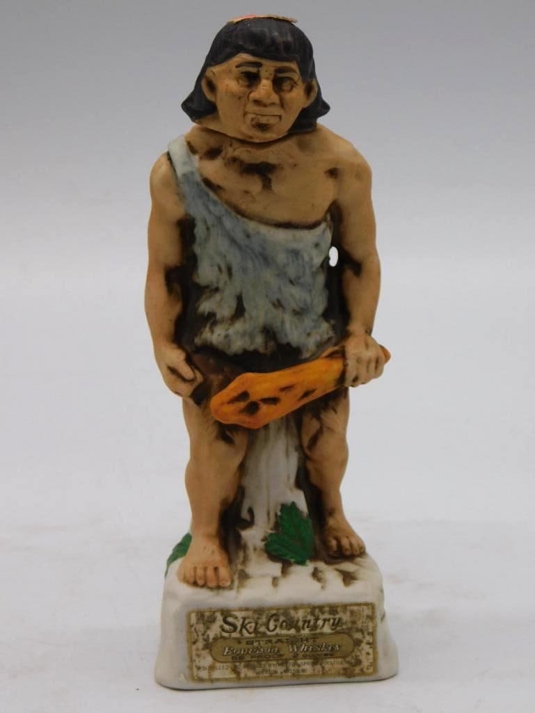 Ski Country Caveman Miniature Decanter: A small Ski Country ceramic decanter modeled as a caveman with club in hand and an animal-skin garment about him, standing on a rock and leaf-textured base. Miniature format, approximately 7 inches
