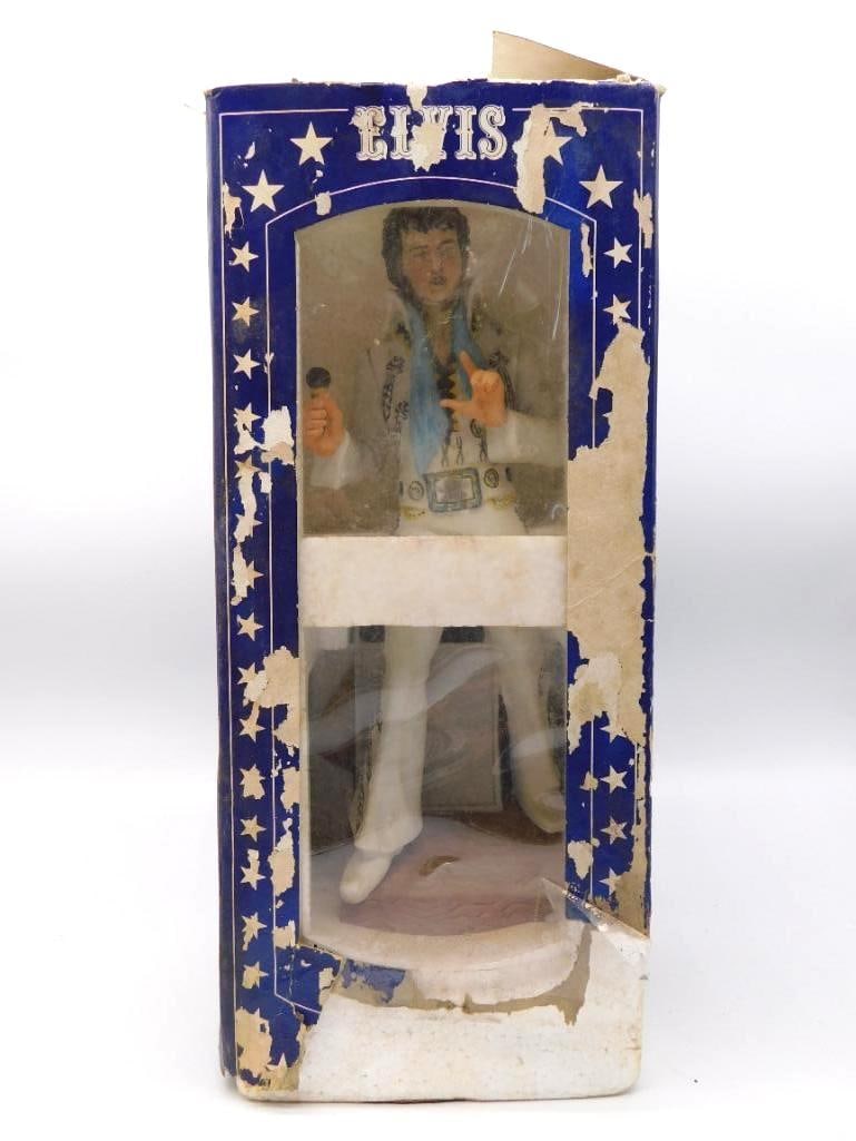 McCormick Elvis Presley 1977 Music Box: A McCormick decanter modeled as Elvis Presley in a white studded jumpsuit, microphone in hand and a blue scarf at the collar. The sculptor gave him a singer's easy stance, and the painter did not