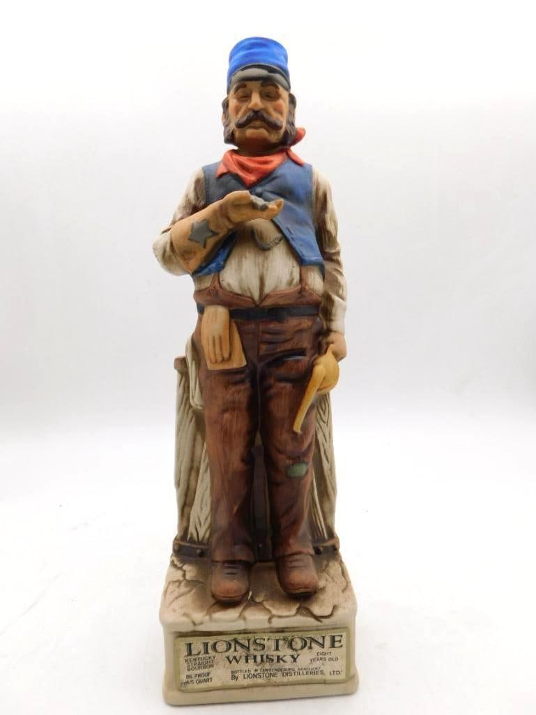 Lionstone Eight Years Old Decanter: A Lionstone bourbon decanter modeled as a mustached tradesman in blue cap and vest, a red neckerchief at his throat, standing before a slatted wooden crate. The bisque finish and quiet coloring suit