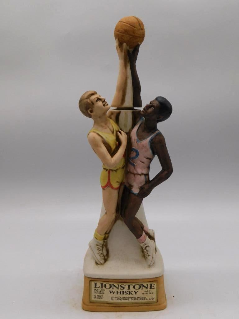 Lionstone Basketball Players Decanter: A larger Lionstone ceramic decanter sculpted with two basketball players, one dribbling and one reaching to block, upon a tall tapered bourbon-bottle form. The sculptor caught the contest fairly.