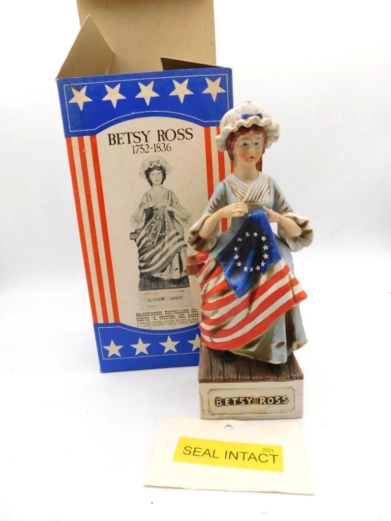 McCormick Betsy Ross Porcelain Decanter: A McCormick Distilling porcelain decanter portraying Betsy Ross at her needle, stitching the American flag, upon a base marked Betsy Ross. Comes with its red, white and blue patriotic shipping box.