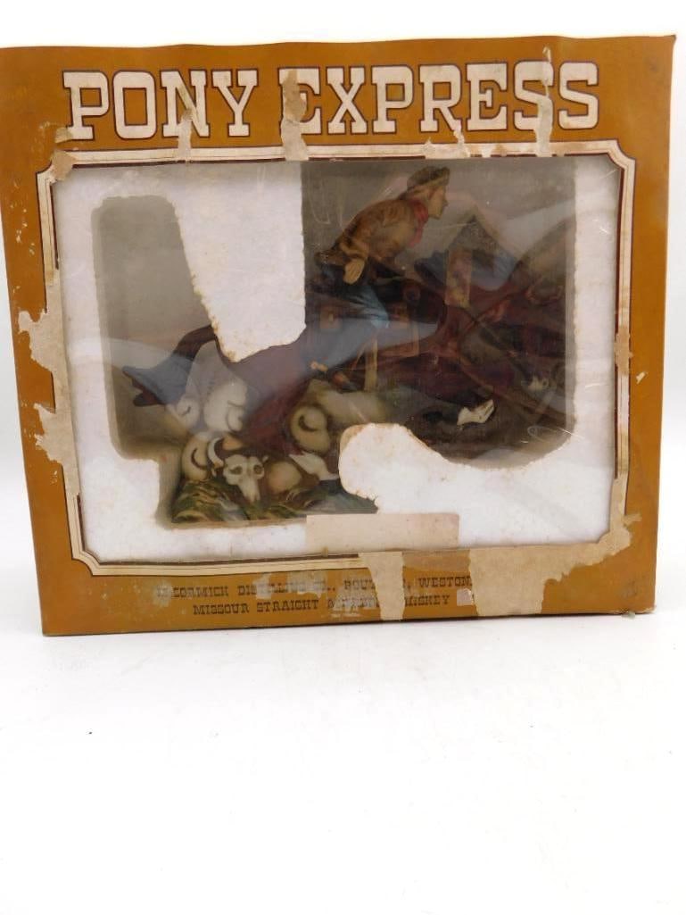 McCormick Pony Express Rider Decanter: A McCormick decanter modeled as a Pony Express rider at full gallop, mail pouches strapped behind him and a longhorn skull among the grass at the horse's feet. The piece remains in its original window