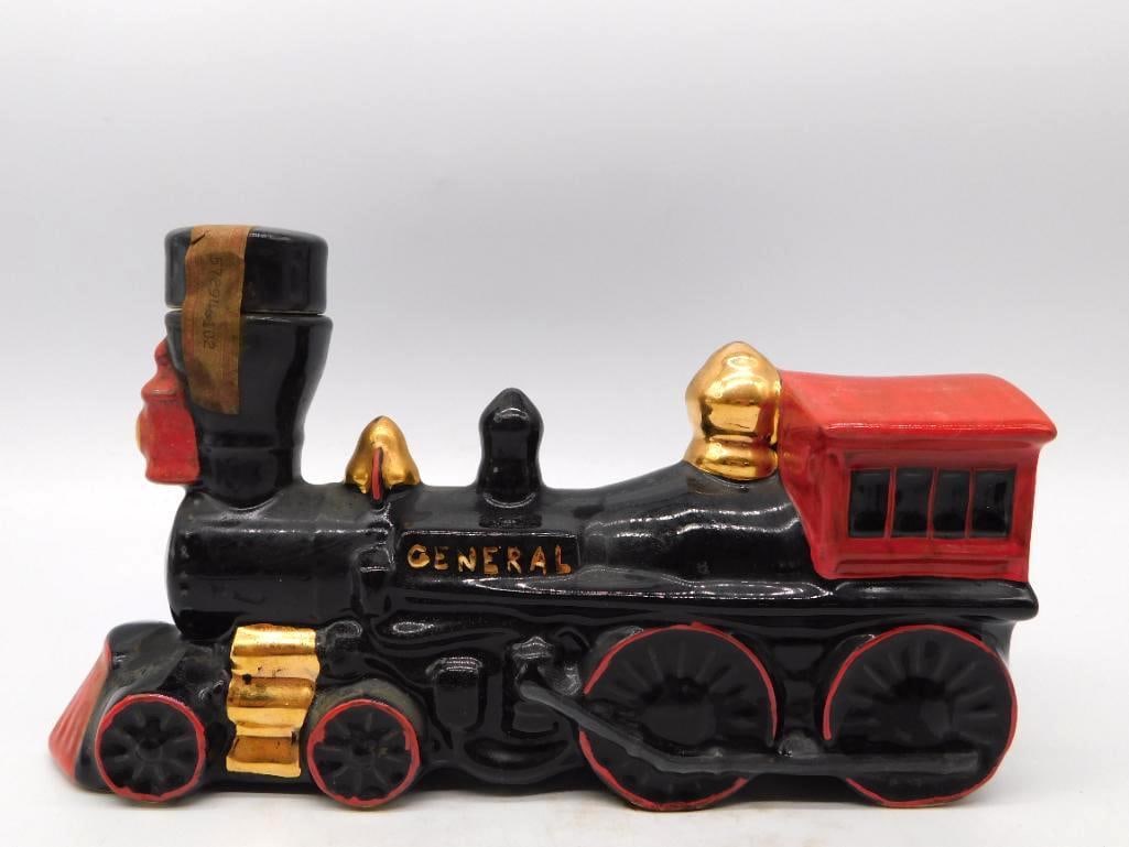 The General Locomotive Decanter in Black: A sturdy decanter modeled as the old wood-burning locomotive The General, its name lettered in gold along the boiler, with gilt bell and steam dome and a bright red cab and cowcatcher. Unmarked as to