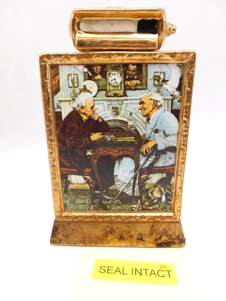 Norman Rockwell Checkers Ltd Ed Decanter: A limited edition ceramic decanter reproducing Norman Rockwell's painting of two elderly men at checkers before the fireside, set in a gold-tone frame with 23K gold trim. Bottled by The Mike Wayne Dis