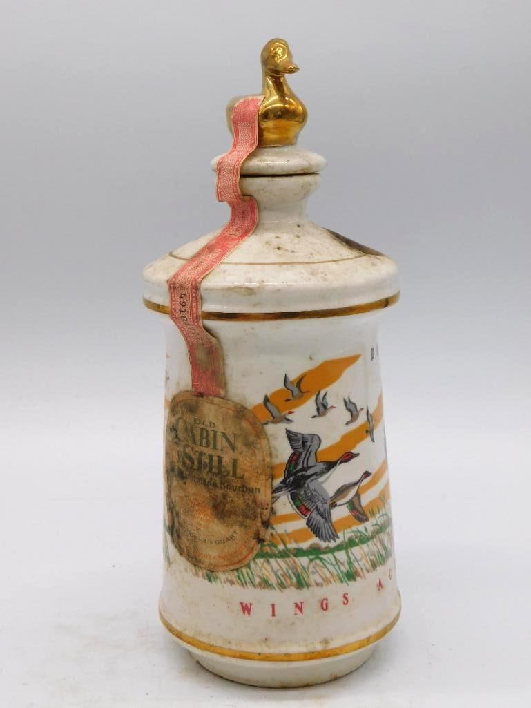 Old Cabin Still Wings of America Duck: A porcelain Old Cabin Still decanter from the "Wings of America" series, hand-painted with flying ducks and topped by a gold duck stopper. Kentucky Straight Bourbon Whiskey. The body and label show