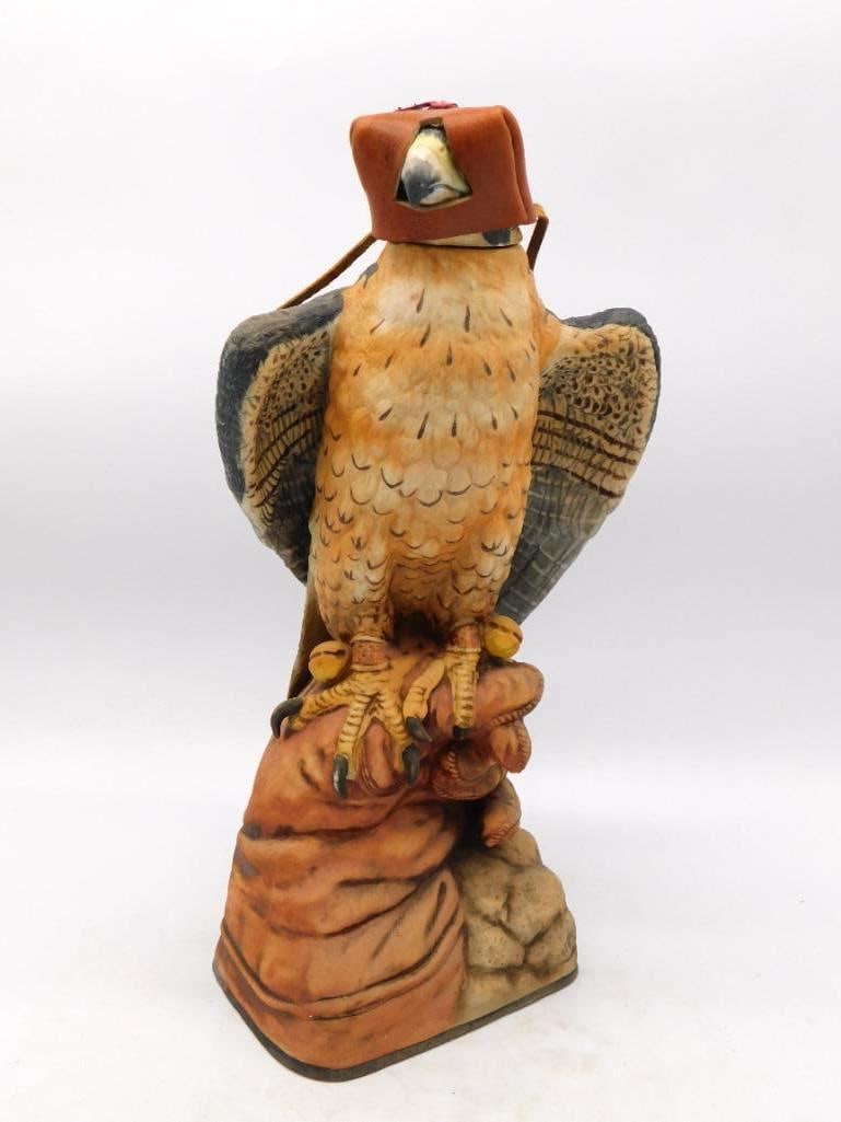 Hooded Falcon on Falconer's Glove: A singular bisque decanter modeled as a hooded falcon perched upon a falconer's gauntlet, fitted with a genuine leather hood and braces. The plumage is finely tooled and the painter carried the barrin