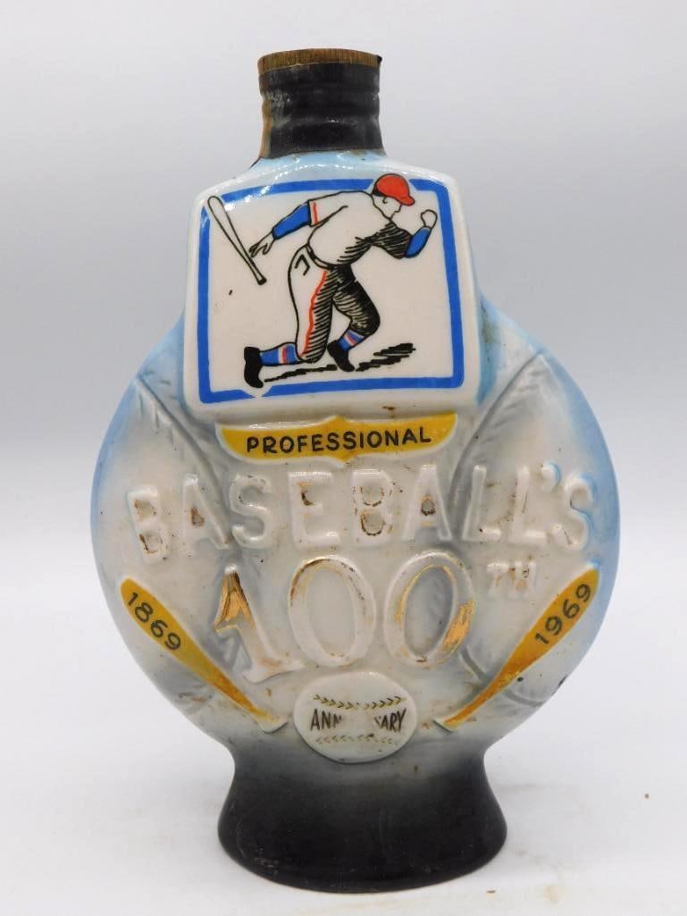 Baseball's 100th Anniv. 1869-1969 Comm.: A ceramic commemorative whiskey decanter marking "Baseball's 100th Anniversary, Professional, 1869-1969," decorated with a vintage ballplayer graphic in a blue and white ribbon design. Dark neck with
