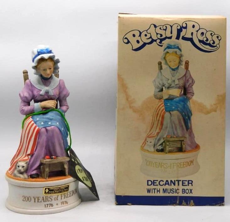 Hoffman Betsy Ross 200 Years of Freedom: A Hoffman Original decanter modeled as Betsy Ross seated in a ladder-back chair, needle in hand and the young flag spread across her lap, a white cat and a workbasket at her feet. The painting is care