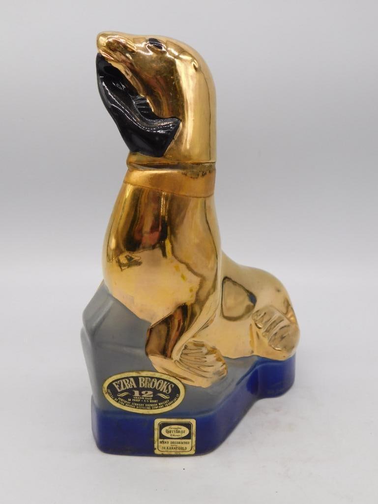 Gold-Tone Eagle Decanter: A gold-tone metal decanter cast as a bald eagle with wings folded, mounted on a rectangular base bearing a small maker's emblem too small to confirm in the photos provided. The seal is intact. See pho