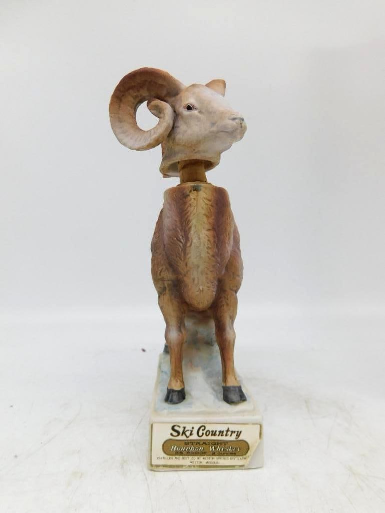 Ski Country Bighorn Ram Decanter, Rocky: A Ski Country decanter modeled as a bighorn ram standing on a snowy ledge, head lifted and horns curled full round. The coat is worked in warm browns against blue-white rock, and the modeling is