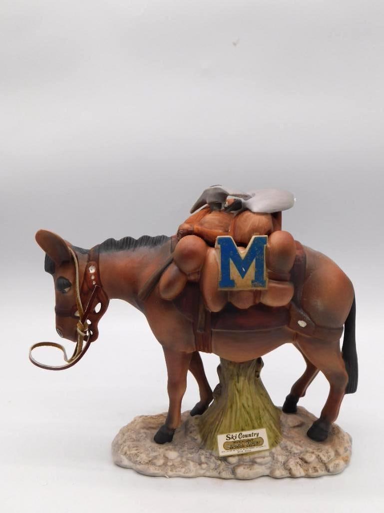 Ski Country Pack Mule Decanter: A Ski Country decanter modeled as a laden pack mule with saddle bags and a blue M blanket, set upon a rocky base. Approximately 9 inches tall as photographed, with minor wear only. The sculptor caught