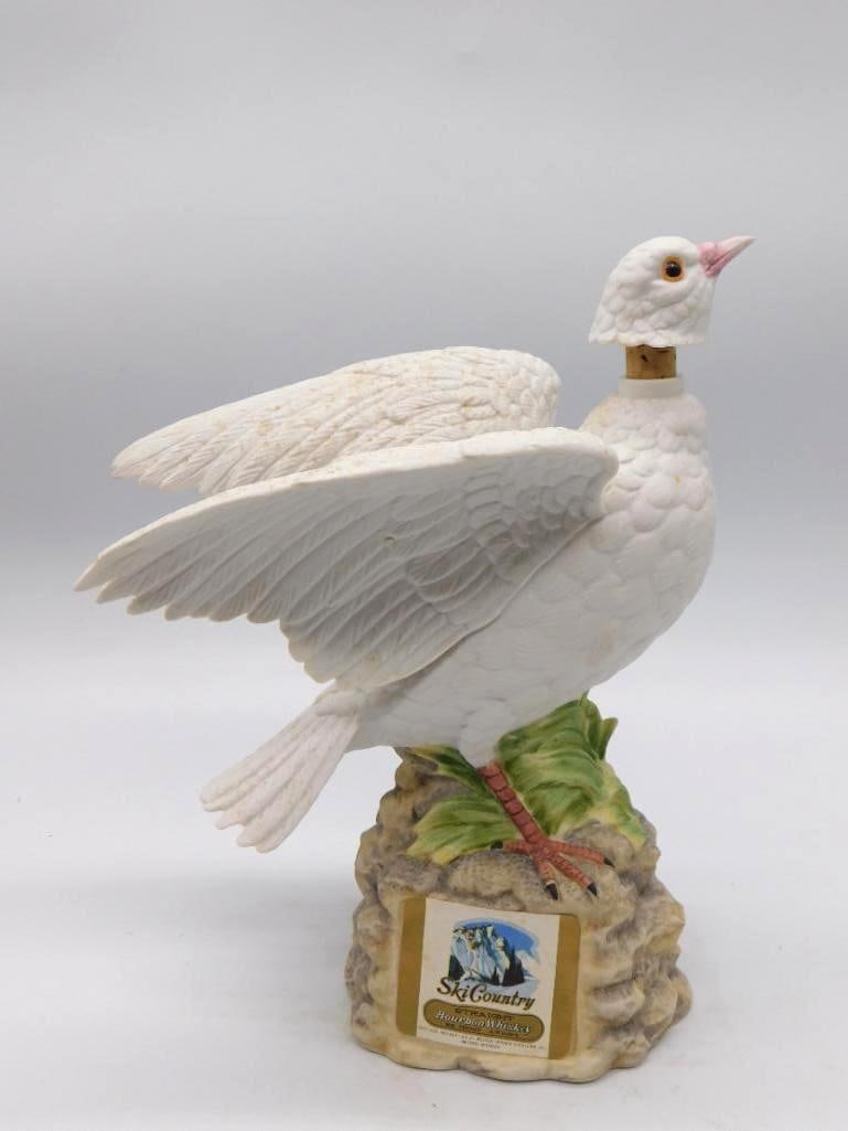 Ski Country White Dove Bourbon Porcelain: A Ski Country porcelain decanter, hand-painted, modeled as a white dove with wings spread above a rocky and foliage base. A trim and peaceable subject, well finished. The original paper label is prese