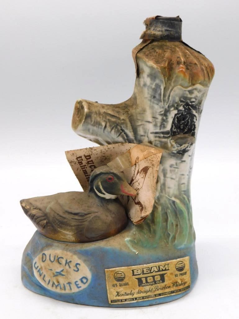 Jim Beam Ducks Unlimited Wood Duck: A Jim Beam ceramic decanter modeled as a wood duck at rest on a tree stump, with a Ducks Unlimited medallion and the printed conservation history tag. Marked Kentucky Straight Bourbon Whiskey and