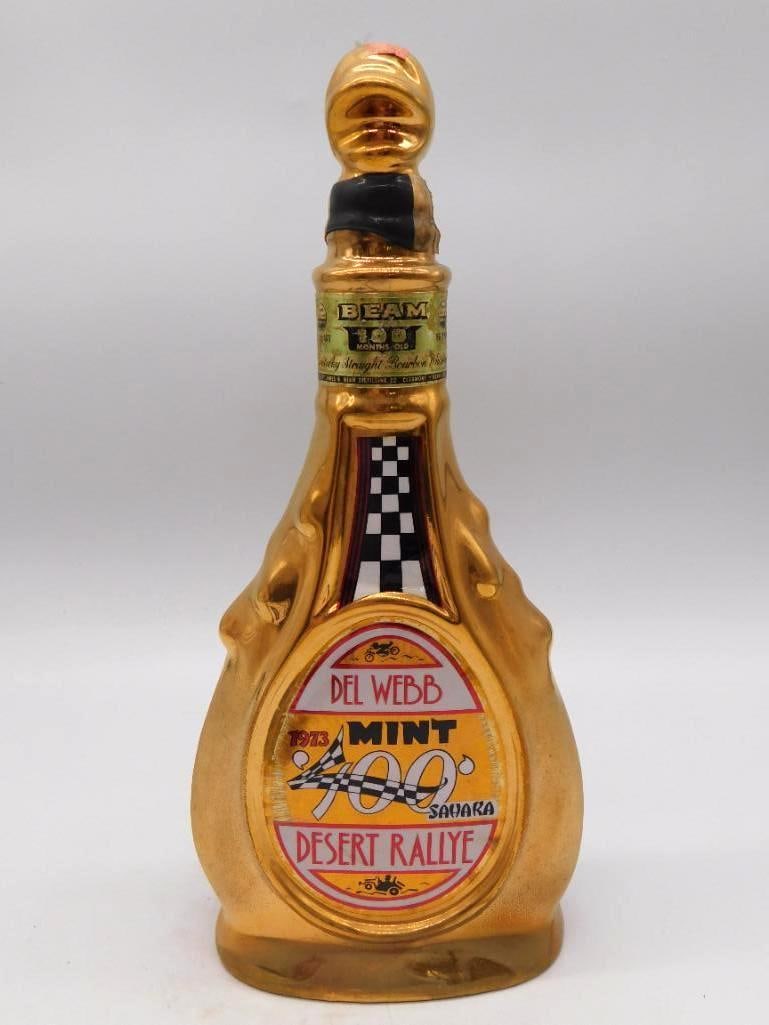 Jim Beam Del Webb Mint 400 Desert Rallye: A gold-glazed Jim Beam ceramic decanter marking the 1973 Del Webb's Mint 400 Desert Rallye, dressed with a checkered-flag racing motif. Kentucky Straight Bourbon Whiskey, 100 months old. A lively