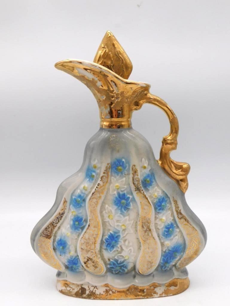 Jim Beam Blue and Gold Ewer Decanter: A handsome Jim Beam ewer with gilded spout and handle rising from a fluted body of blue and white. Hand-painted flowers wander the sides, and the gilding keeps its brightness. Stands approximately 10.