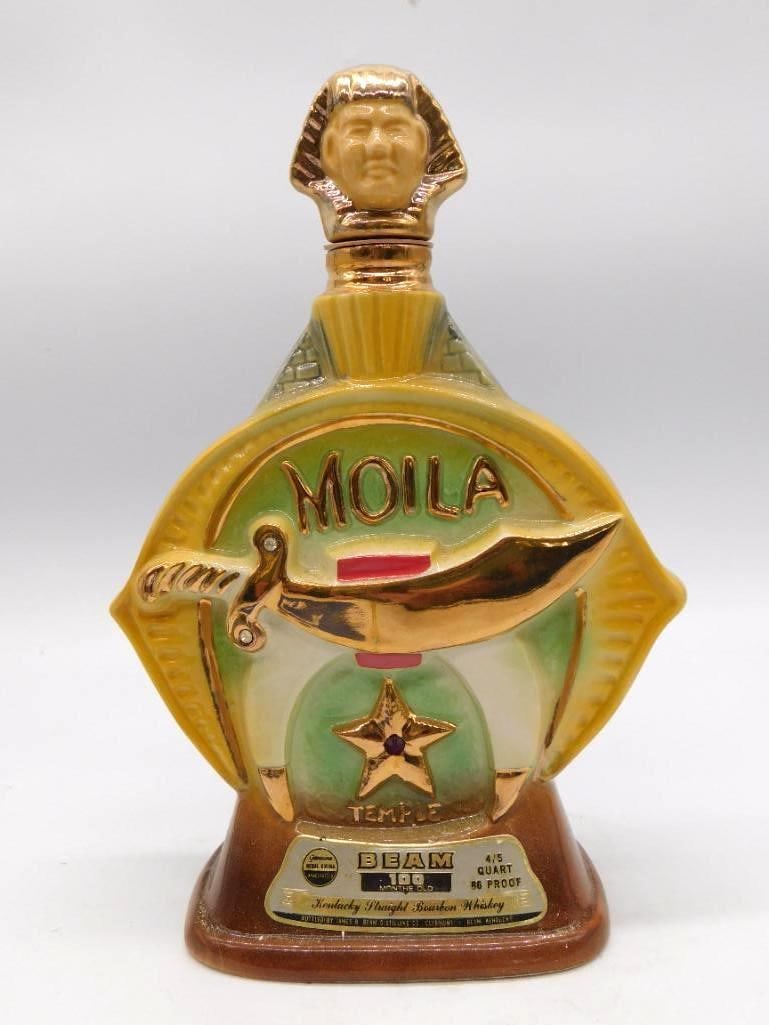 Jim Beam Moila Shrine Temple Ceramic: A Jim Beam ceramic Shriner decanter for Moila Temple, worked in gold and green with crescent, star and scimitar medallions upon both faces. The stopper is modeled as a sultan, a jaunty finish to a