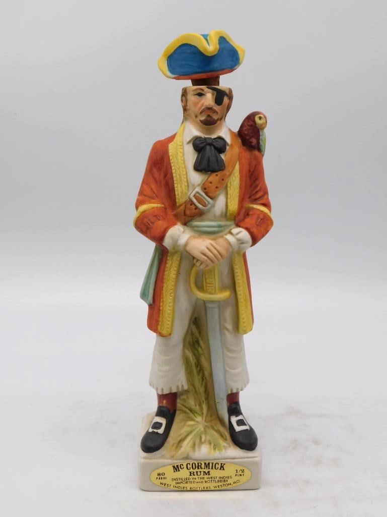 McCormick Rum Buccaneer with Parrot: A jaunty McCormick decanter modeled as a buccaneer in a scarlet coat, eye patched and cutlass in hand, a red parrot perched at his shoulder and a blue tricorn hat serving as the stopper. The painter d