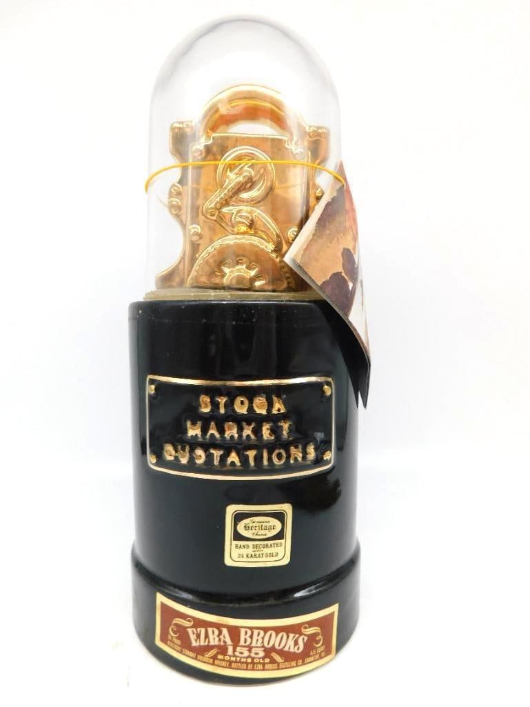 Ezra Brooks Stock Market Ticker 24 Karat: An Ezra Brooks Heritage China decanter hand-decorated in 24 karat gold and modeled as a stock market ticker beneath a glass-look dome, finished with a gold quotation plate. It retains its original