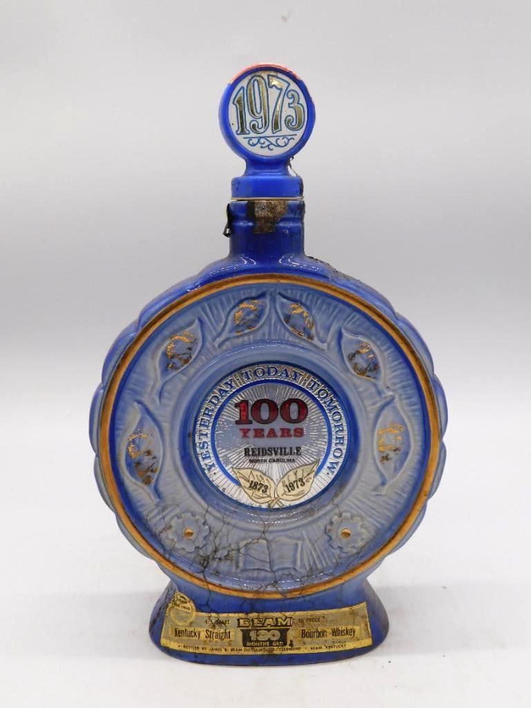 Jim Beam Reidsville North Carolina: A Jim Beam ceramic decanter in cobalt blue and gold, struck for the 1873-1973 Centennial of Reidsville, North Carolina, with molded medallions upon both faces and a stopper dated 1973. A Kentucky