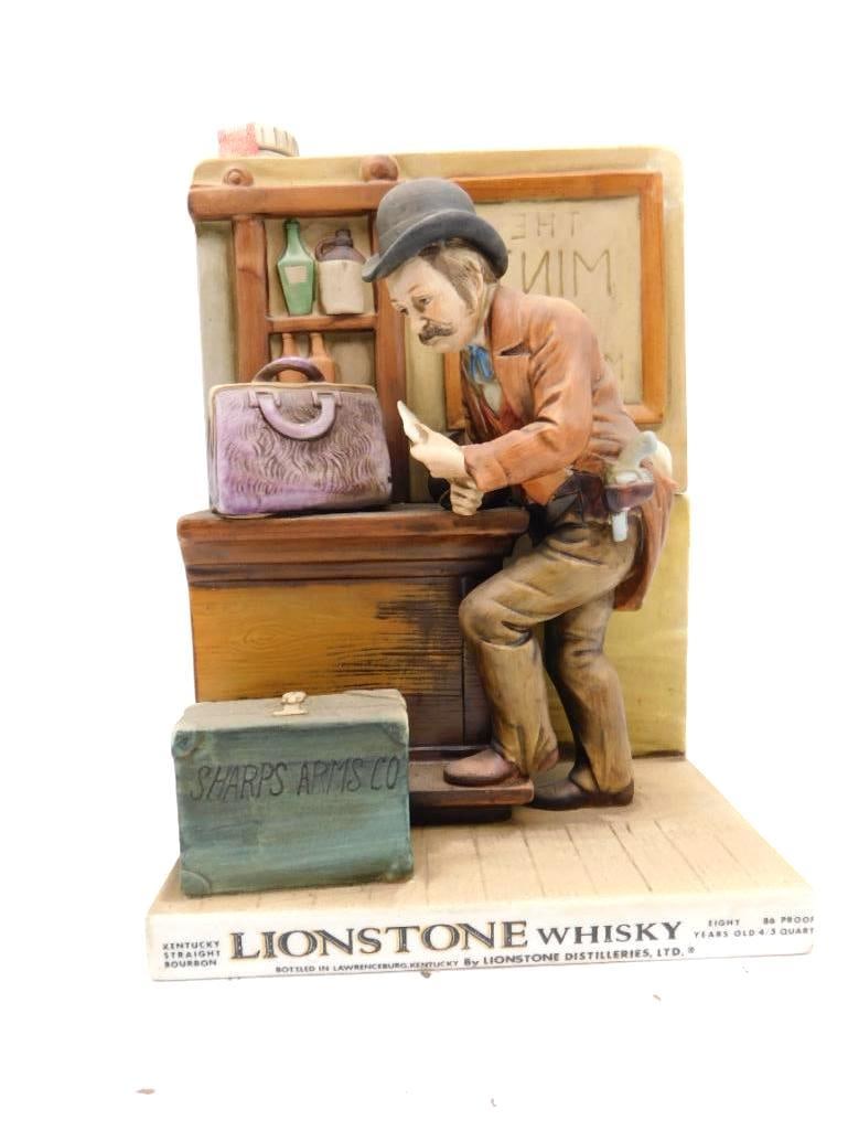 Lionstone Whiskey Sharps Arms Co: A Lionstone Kentucky Straight Bourbon Whiskey porcelain decanter showing a man in a bowler hat leaning at a desk over a document, a Sharps Arms Co. case and satchel set below on a brick-and-wood jug