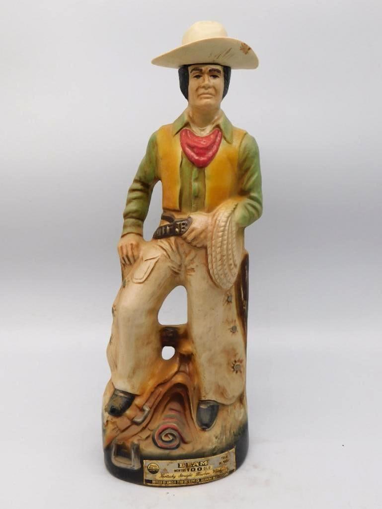 Jim Beam Regal China Cowboy Decanter: A capital Jim Beam bottle modeled as a cowboy at his ease, one boot up on a weathered stump, lariat in hand and a red bandanna knotted at his throat. The palette is soft — sage, ochre and cream — 