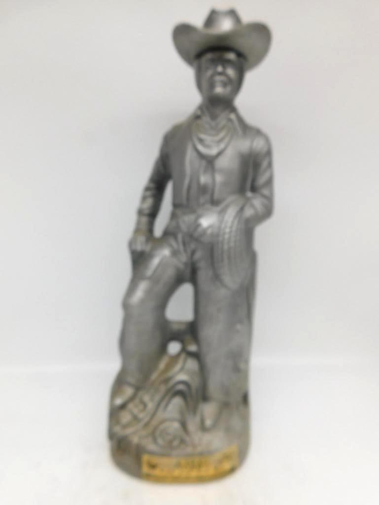 Silver-Finished Cowboy Decanter: A cowboy decanter finished overall in a silvered metallic coat, the man leaning easy against a fence post with lariat in hand and his broad-brimmed hat serving as the stopper. The modeling is sharp