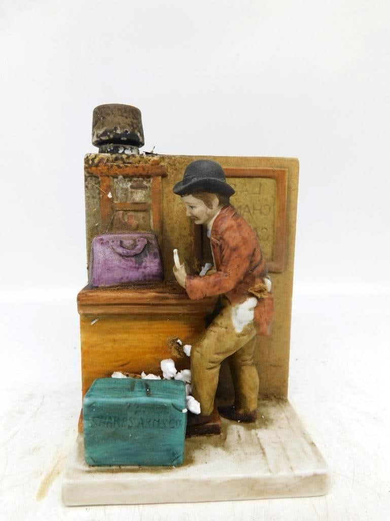 Old West Sharps Arms Co. Shop Scene: A small decanter modeled as an Old West shop scene, a clerk in bowler hat and red coat bent over his counter with a purple valise at his elbow and a green crate lettered SHARPS ARMS CO. at his feet. T