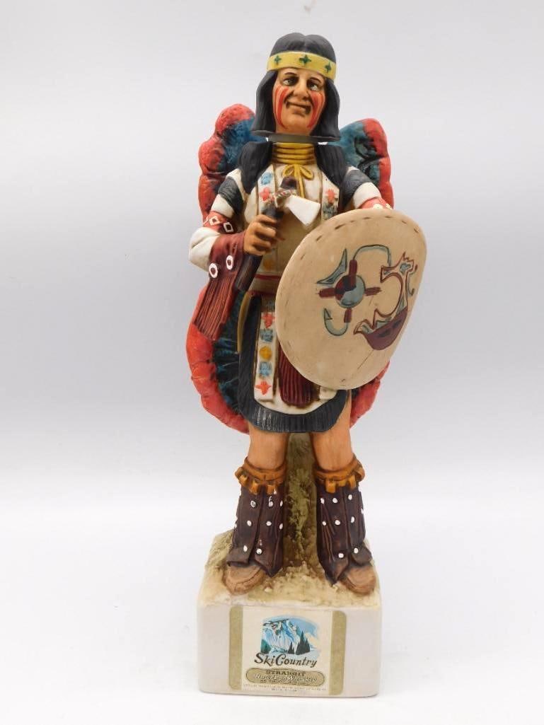 Ski Country Native American Shield: A Ski Country Bourbon Whiskey decanter sculpted as a Native American shield dancer in ceremonial dress, the feathered bustle spread wide and a war axe held aloft. The painter did not stint on the