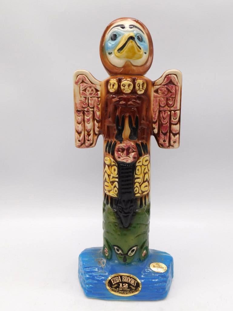 Ezra Brooks Northwest Coast Totem Pole: An Ezra Brooks ceramic decanter shaped as a Northwest Coast totem pole, its carved thunderbird head and mask motifs worked in brown, red and cream above a blue rock-form base. No small feat of the mol