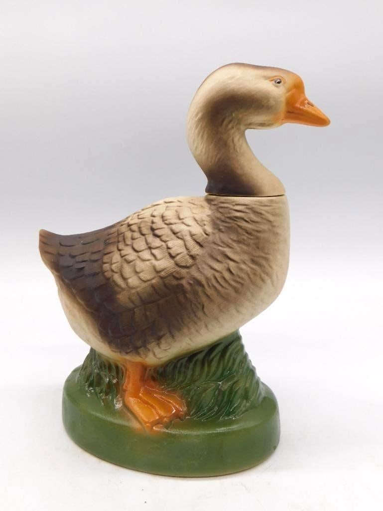 Ceramic Goose Decanter on Grassy Base: An unmarked ceramic decanter modeled as a standing goose upon a green grassy base, naturally colored with an orange bill and feet. A trim and lifelike bird, approximately 9 inches tall, with no chips
