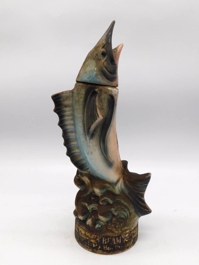 Jim Beam Leaping Marlin Ceramic Decanter: A Jim Beam ceramic whiskey decanter in the form of a leaping marlin, caught mid-arc with a spirited turn of the tail. The Beam brand label is to the base. Stands approximately 12 inches tall. See