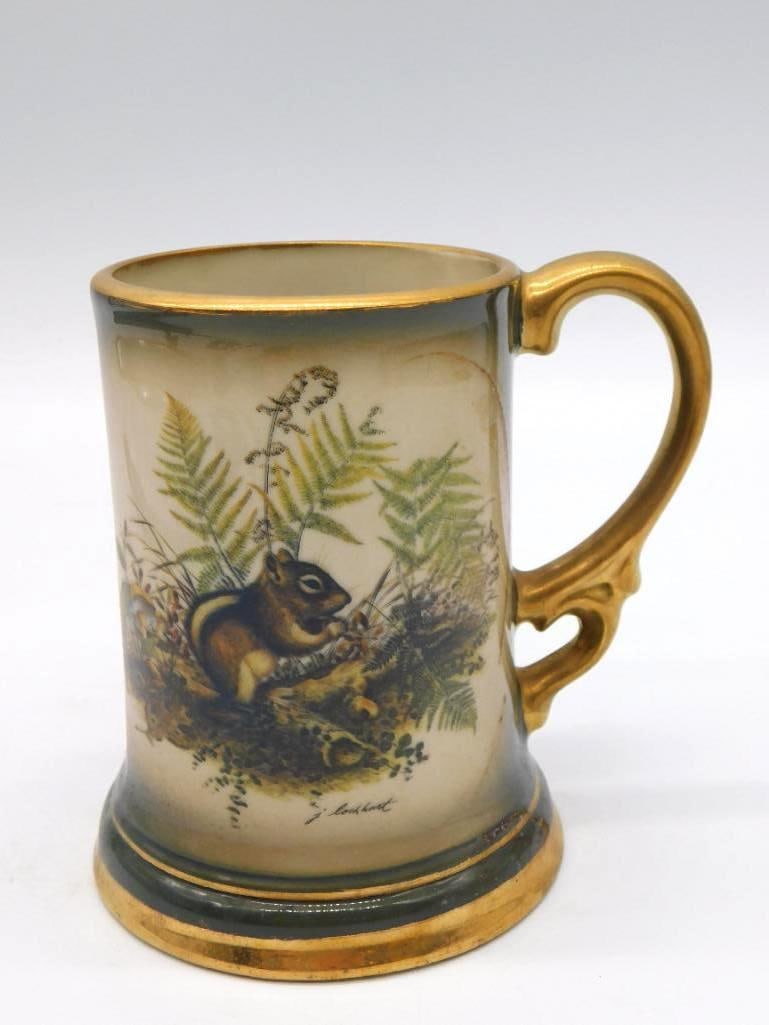 Hand-Painted Porcelain Squirrel and Fern: A porcelain tankard with a gilt handle, hand decorated with a squirrel among ferns and carrying an artist's signature to the scene. Well-turned work, and the painter had a shrewd eye for the