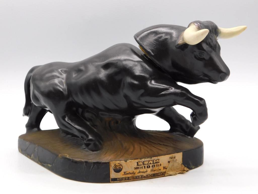 Jim Beam Black Angus Bull Decanter, 100: A Jim Beam decanter modeled as a Black Angus bull at the charge, glossy black with ivory horns, mounted upon a wood-grain effect base. A commanding little beast, ably sculpted. Carries the Beam 100 Mo