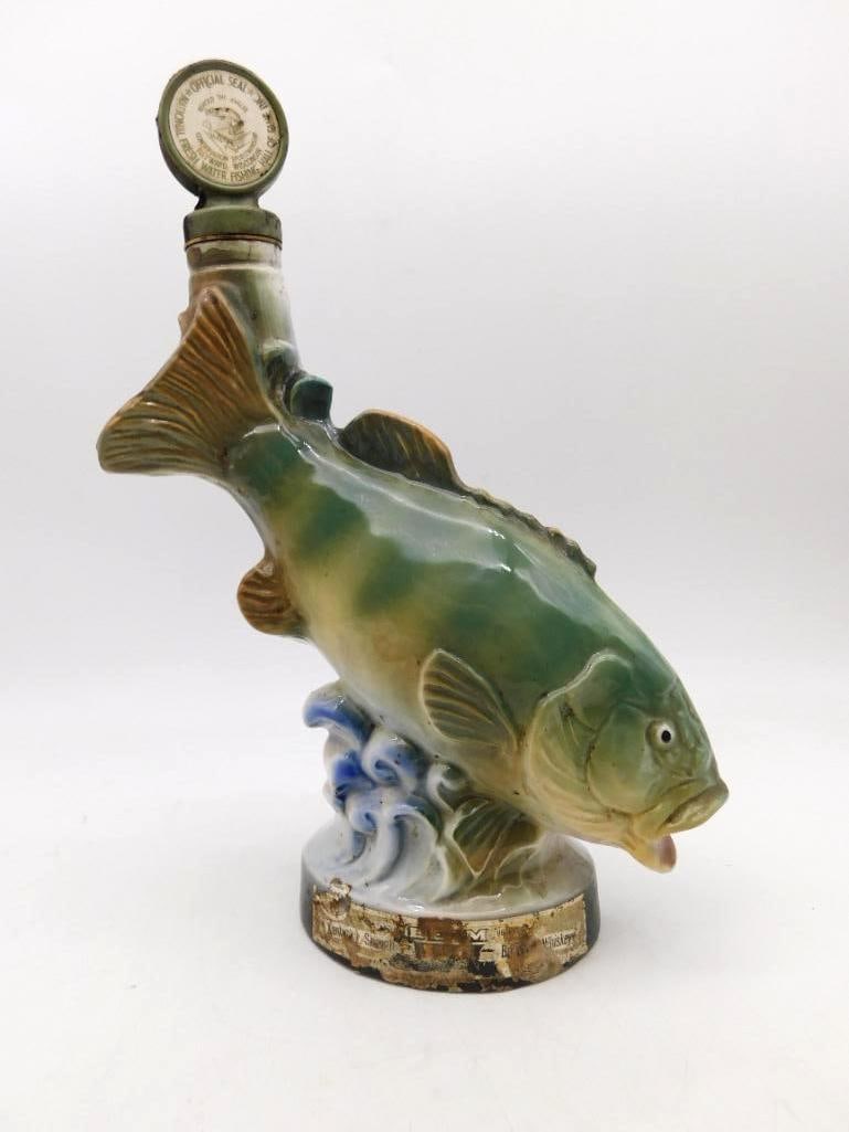Jim Beam Leaping Game Fish Decanter on: A Jim Beam decanter modeled as a game fish breaking clear of the water, its body arched above a cresting blue and white wave. The glaze runs green to gold along the flank, and the fins and scales are